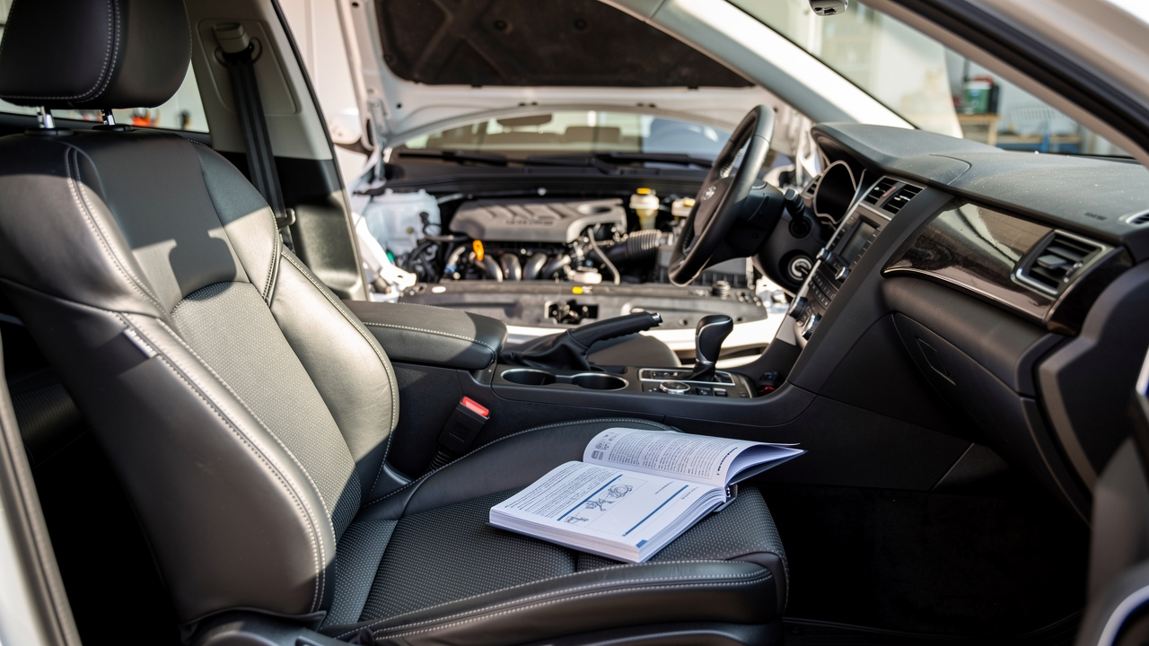Inspection rapprochée d’une berline routière d’occasion : focus sur les sièges, le moteur sous le capot et un carnet d’entretien posé à côté