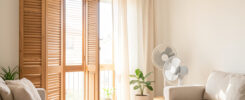 Intérieur lumineux d’un appartement en période de forte chaleur, avec volets fermés, rideaux clairs et ventilateur discret dans une ambiance estivale réaliste.