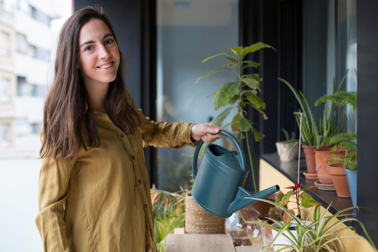 Une personne arrose des plantes vertes sur le balcon de son appartement.